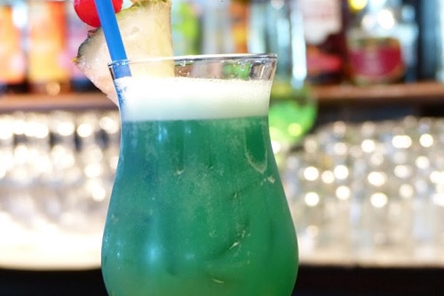 Another Day in Paradise Rum Cocktail Close Up of a Green Cocktail Garnished with a Pineapple Wedge and a Cherry