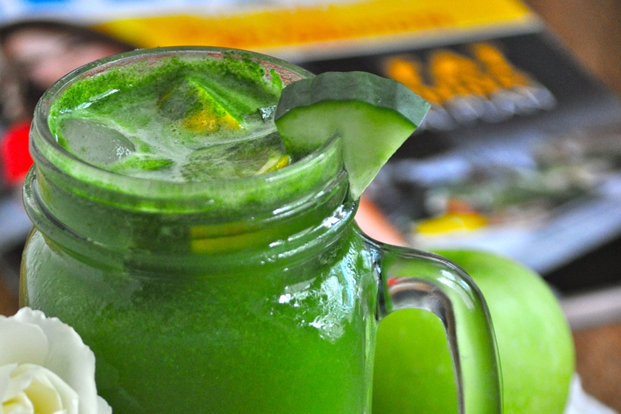 Jillian Michael's Green Juice Recipe Close Up of a Green Juice with a Cucumber Wedge on The Rim and a Jillian Michaels Book in the Background