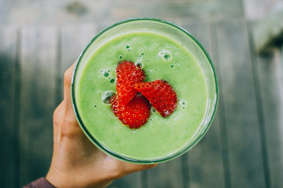 Jillian Michaels Snacks Recipes Overhead View of a Green Smoothie Topped with Raspberries Being Held by a Person's Hand