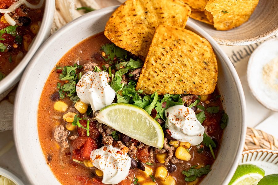 Crockpot Taco Soup Recipe Close Up of a Bowl of Taco Soup Garnished with a Lime Wedge, Sour Cream Dollops, and Two Tortilla Chips