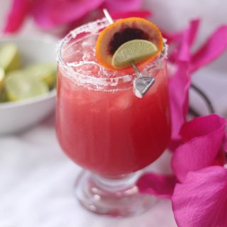 Blood Orange Margarita Recipe In a Glass Next to Flowers and a Small Dish with Lime Slices Inside