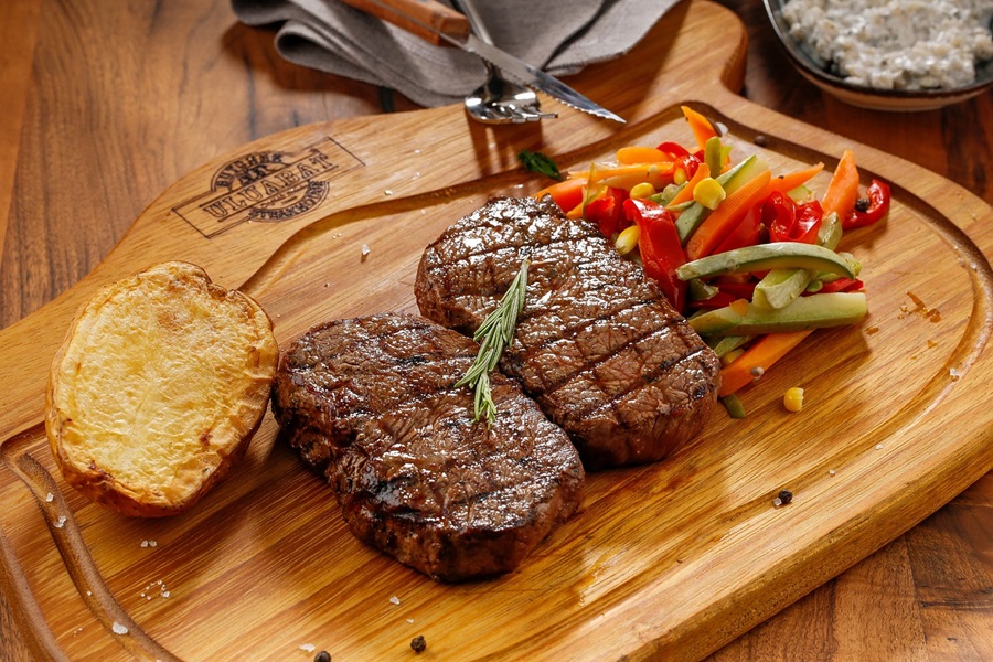 Paleo vs Keto Two Cuts of Beef with Roasted Peppers on a Wooden Cutting Board